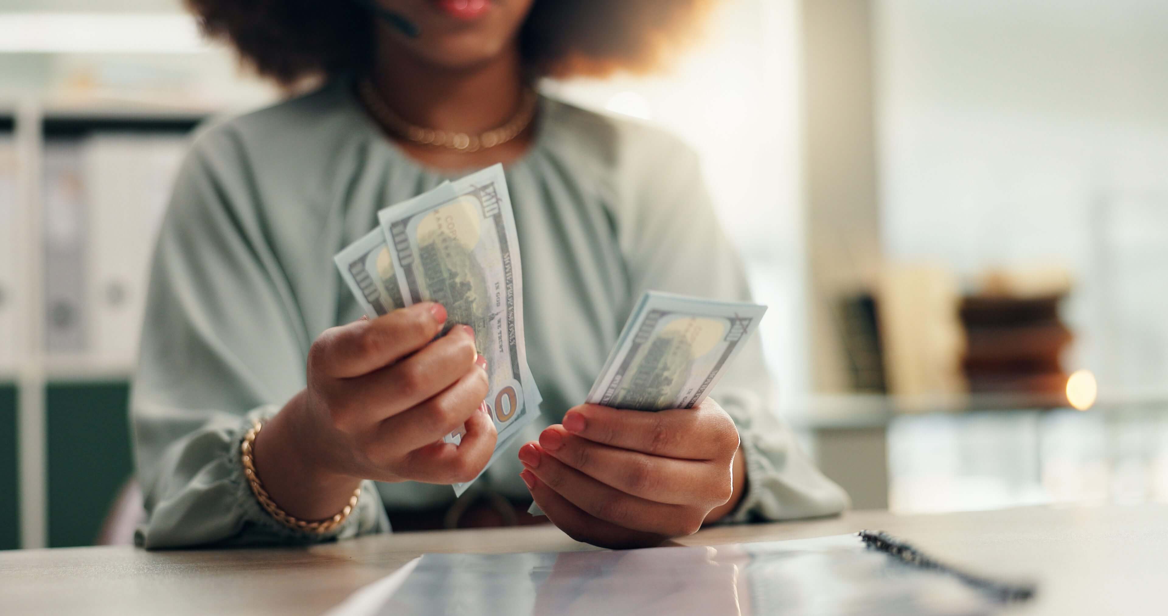 Person counting a stack of US dollar bills indoors.