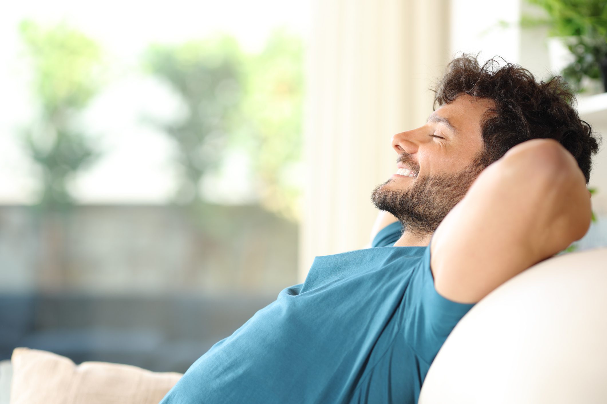 A man relaxing on a couch with eyes closed and a smile.